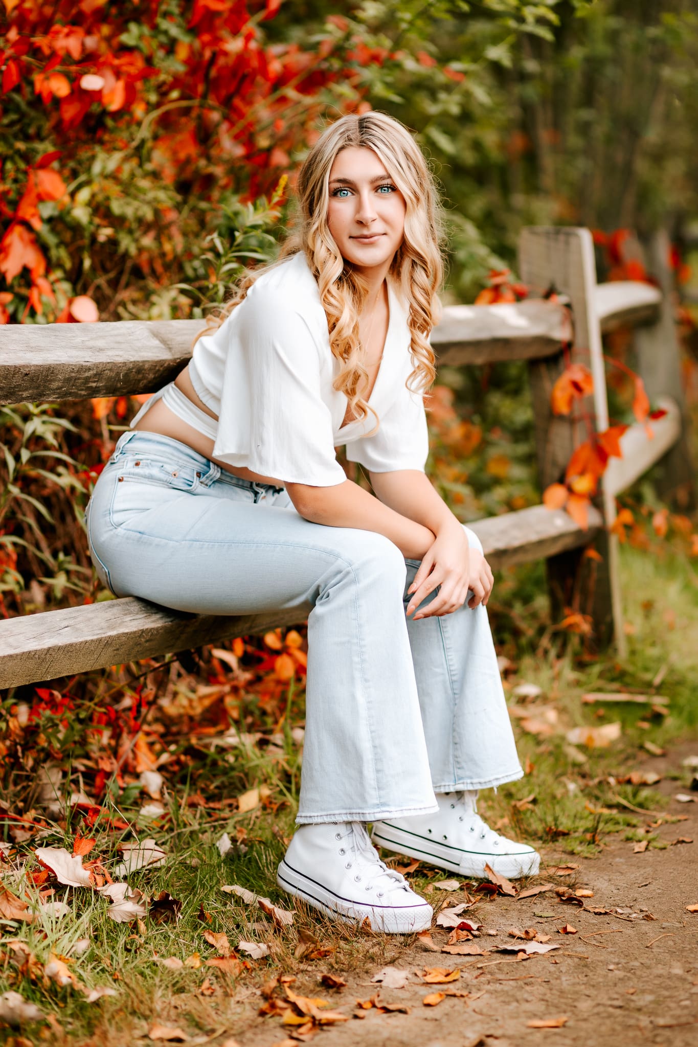 Fall season photo session for s senior girl who is sitting on a fence and gazing at the camera.