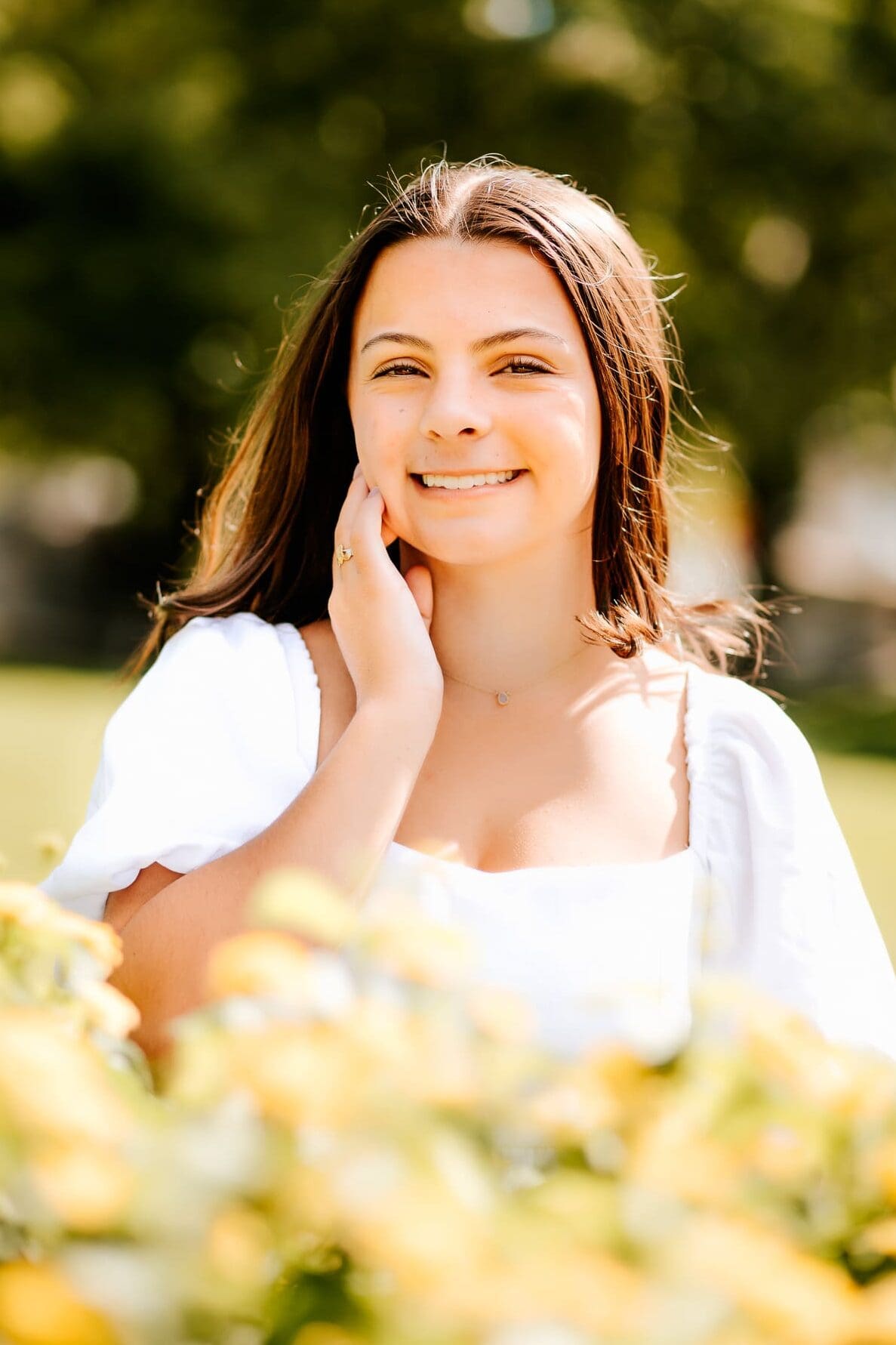 Beautiful glowing senior girl posing with the glow of the summer sun on her face for her senior photos.