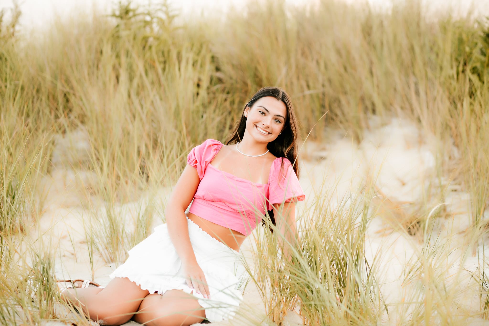High school senior girl sitting in the dunes of a beach during her senior photo session.