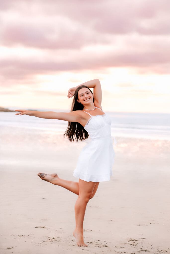 Senior girl posed in a dance position on the beach during sunset during her senior photo session in Massachusetts.