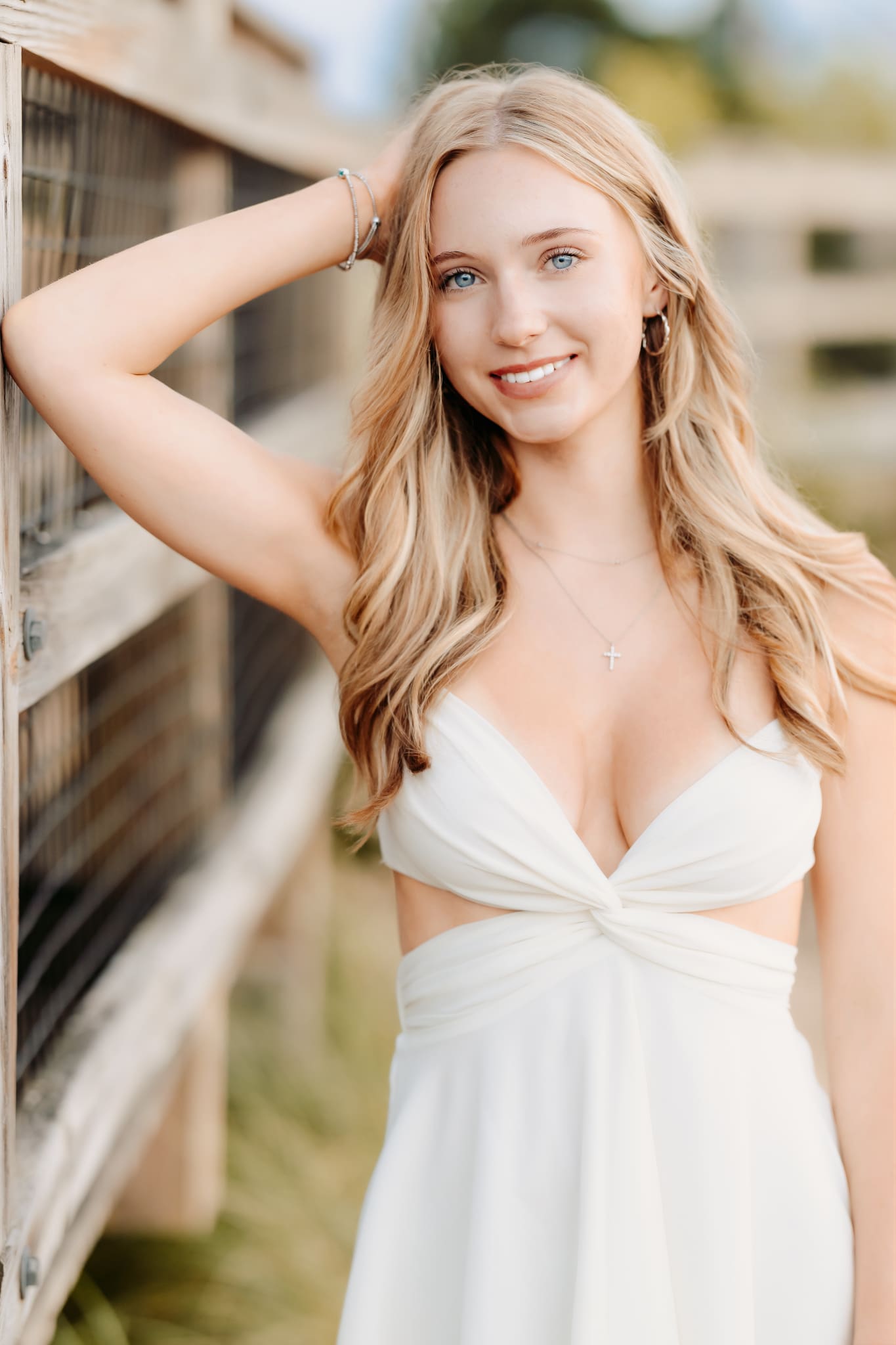 Summer season on the beach is the perfect backdrop for this senior girl standing along a railing for her senior photos.