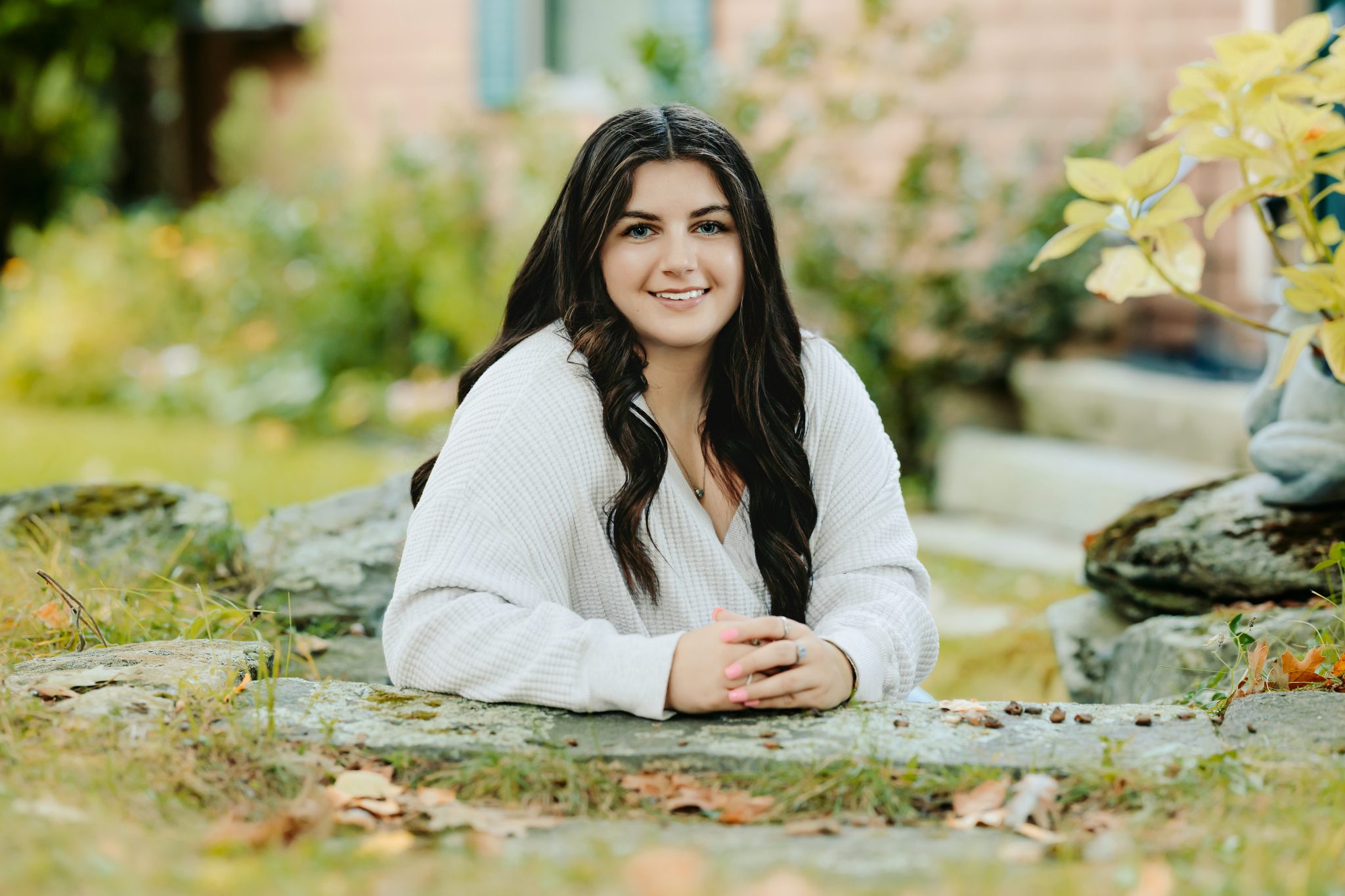 High school senior girl sitting for her senior photos in front of her family home on a lake in New Hampshire.