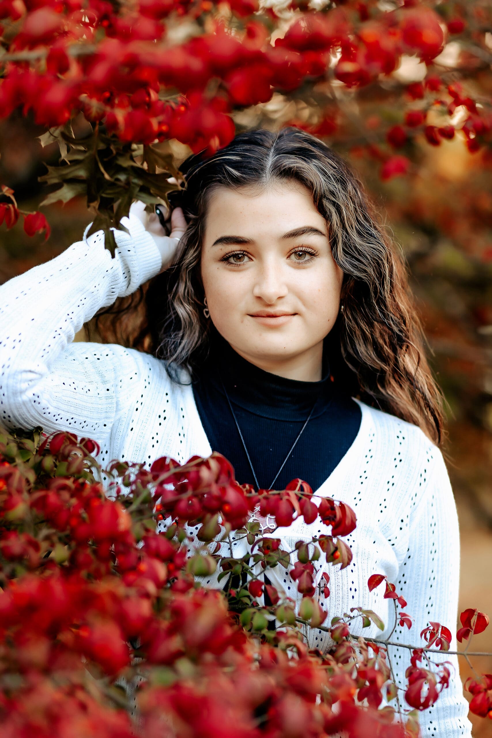 Senior girl standing among the glowing red leaves of Fall during her senior photo session.