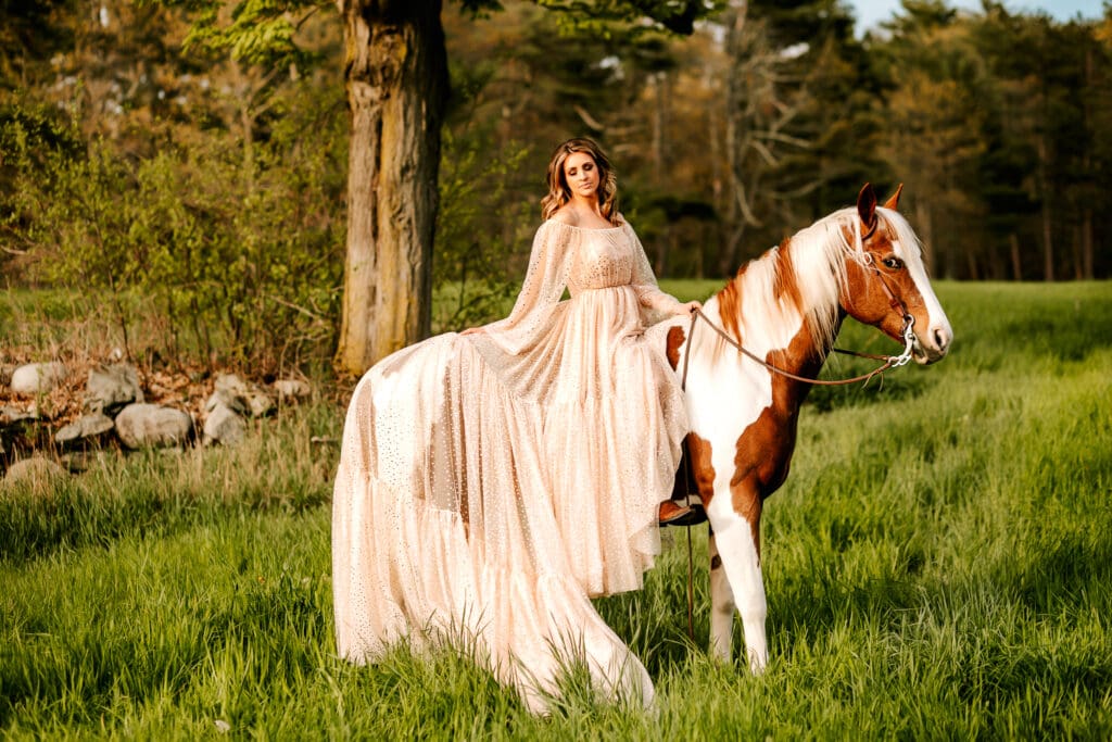 Photo of a female in a flowing dress sitting on a horse in a perfectly lush green field location.