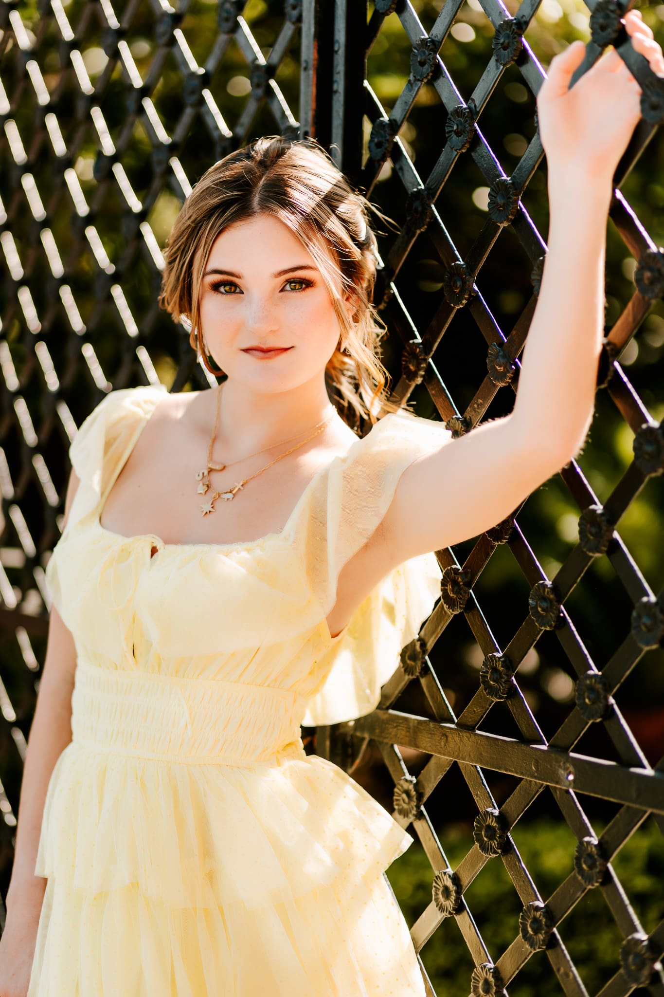 Senior girl standing by a gate in downtown in her favorite dress for her senior photos.