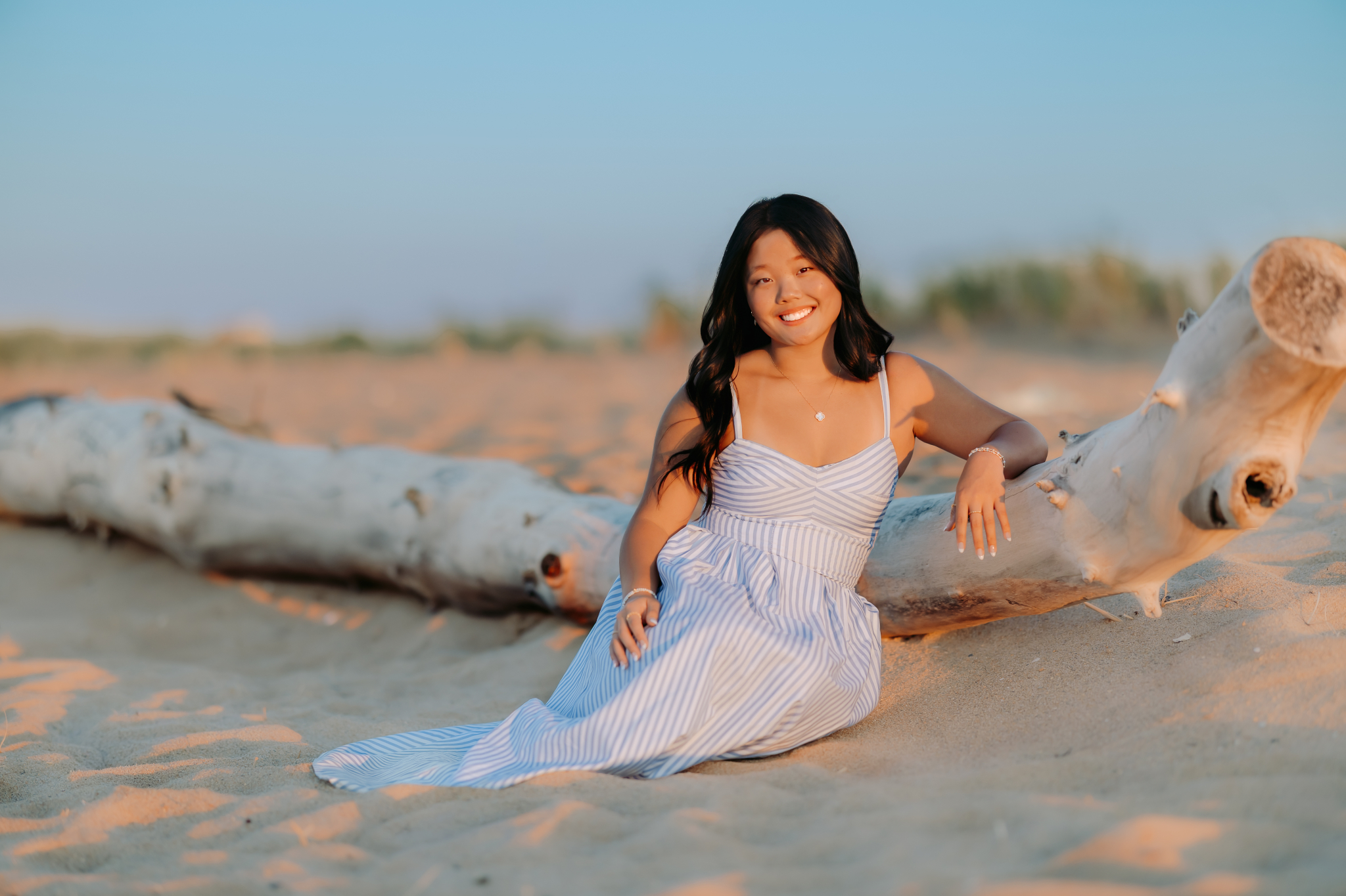 Gorgeous golden hour photo of a high school senior girl leaning on a giant driftwood log in Newburyport, MA