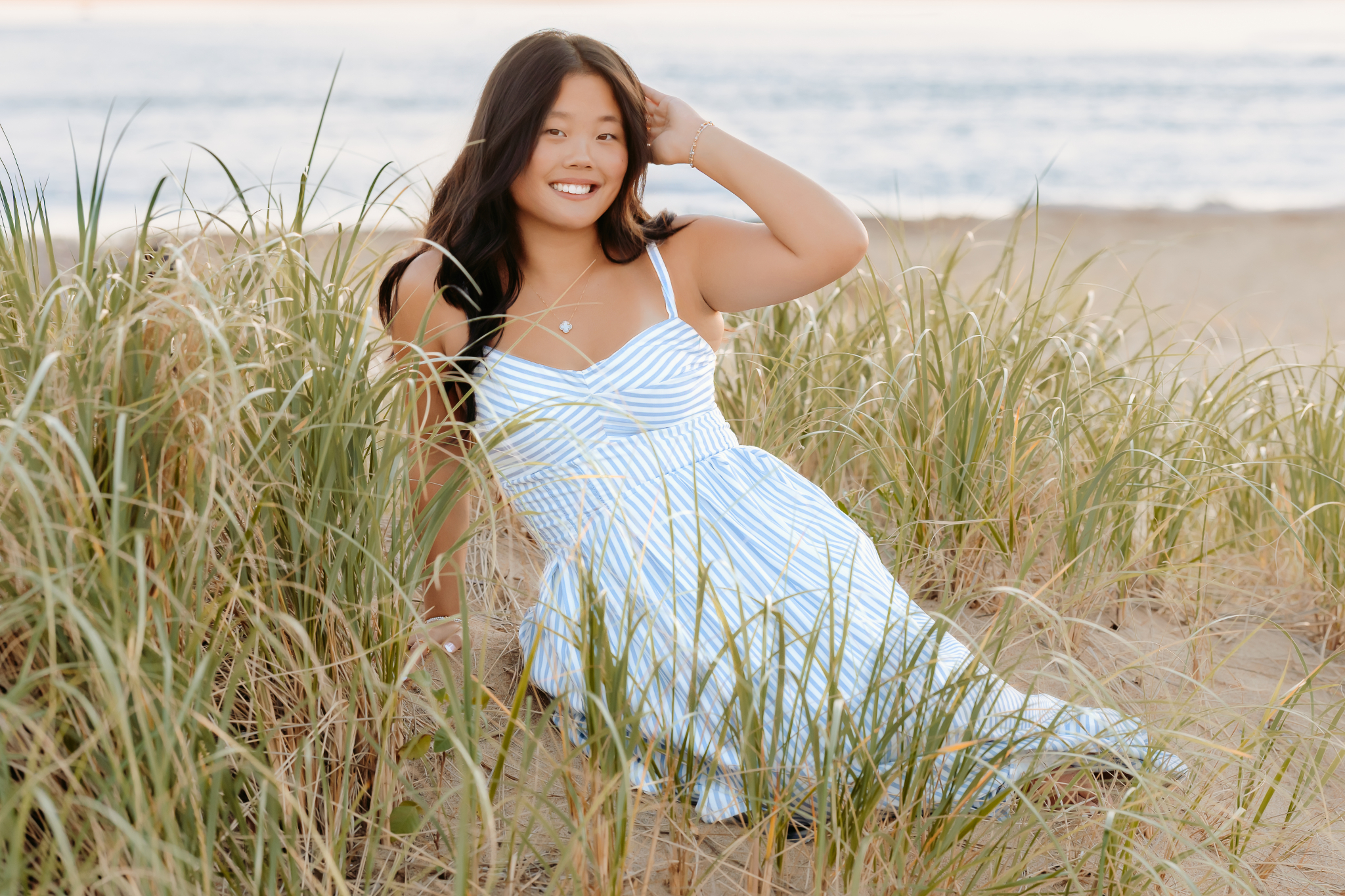 Senior girl sitting on the dunes of Plum Island beach posing for her senior photos.