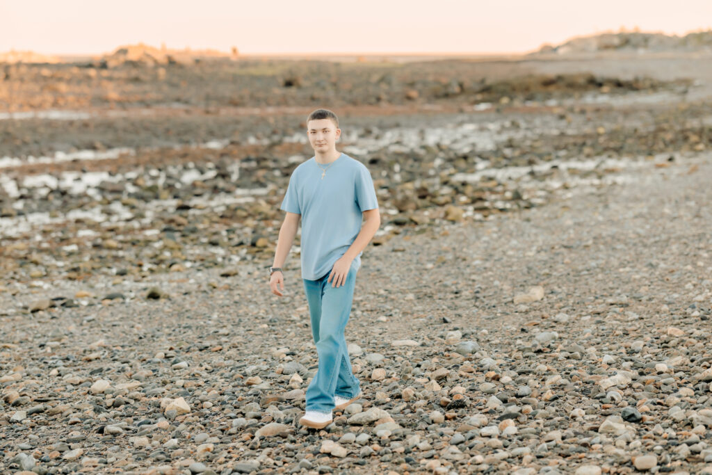 High school senior walking along a rocky New England beach during his senior photo session