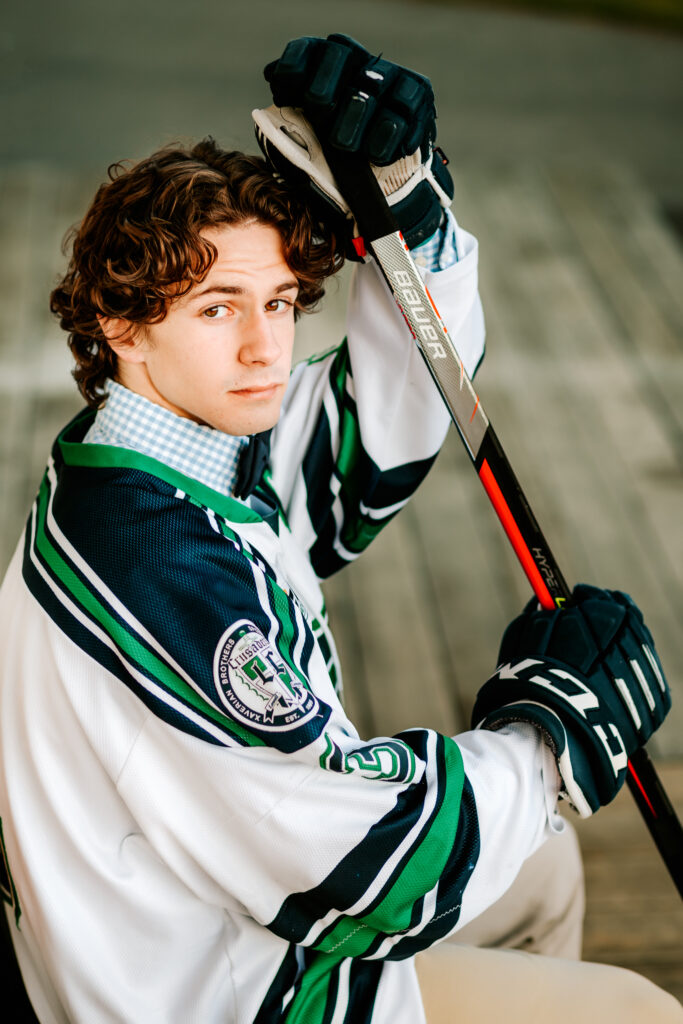 High school hockey player posing in his uniform with his hockey stick during senior photos, Lowell Catholic High School, MA