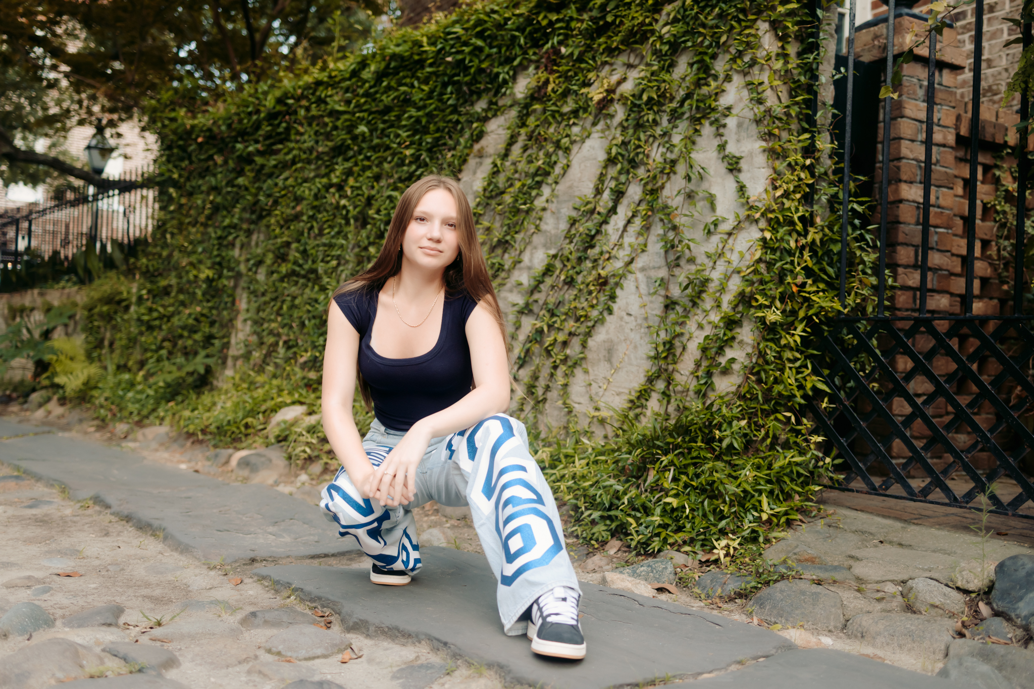 Senior girl posing in front of an ivy wall wearing her Class of 2026 decorated denim.