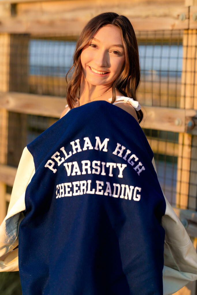 High school senior holding her varsity cheerleading jacket during her senior photo session, Plum Island, Newburyport, MA