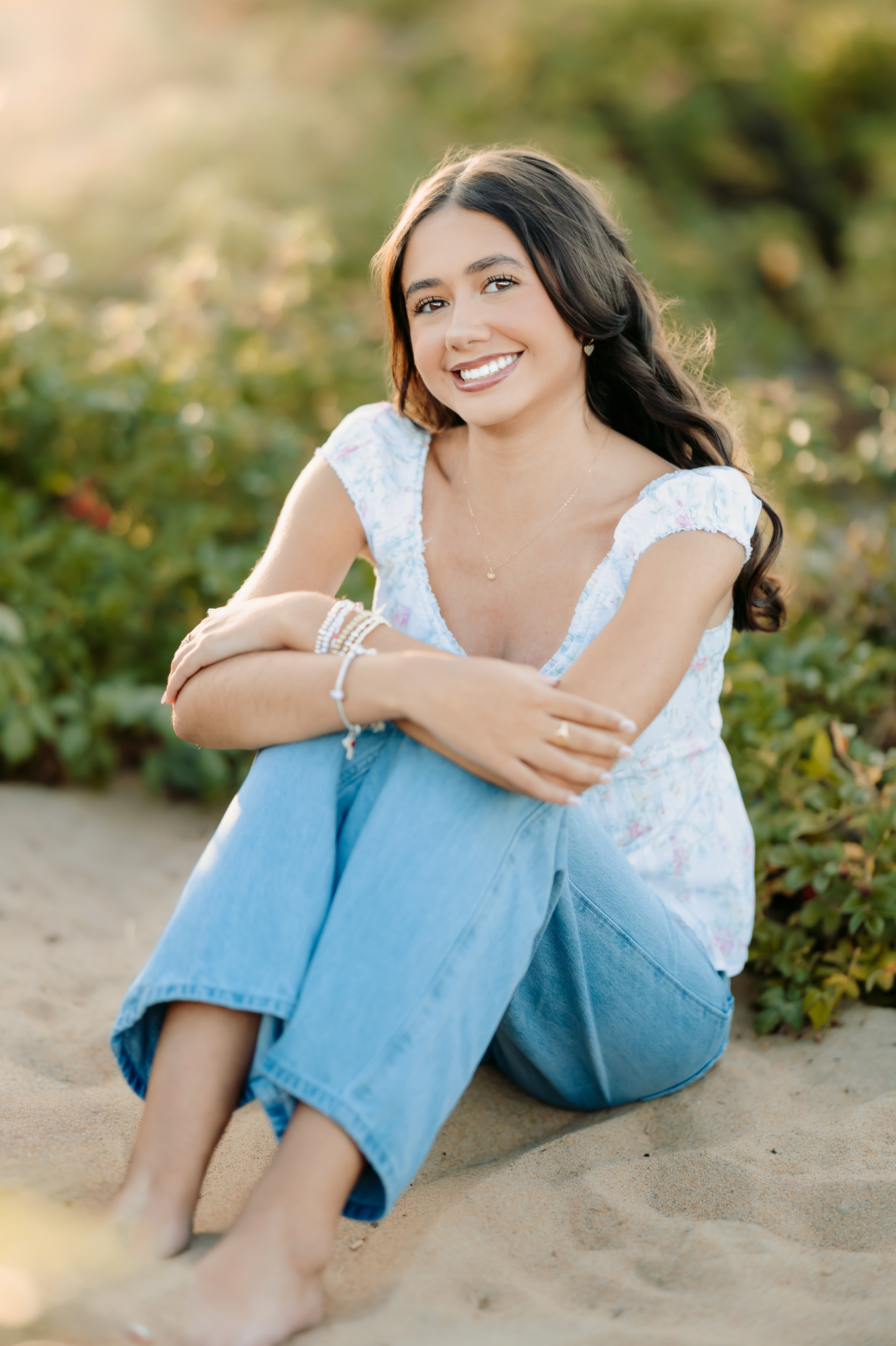 Smiling high school senior girl dressed in a floral white top and wide-leg denim jeans o the beach in Newburyport, MA