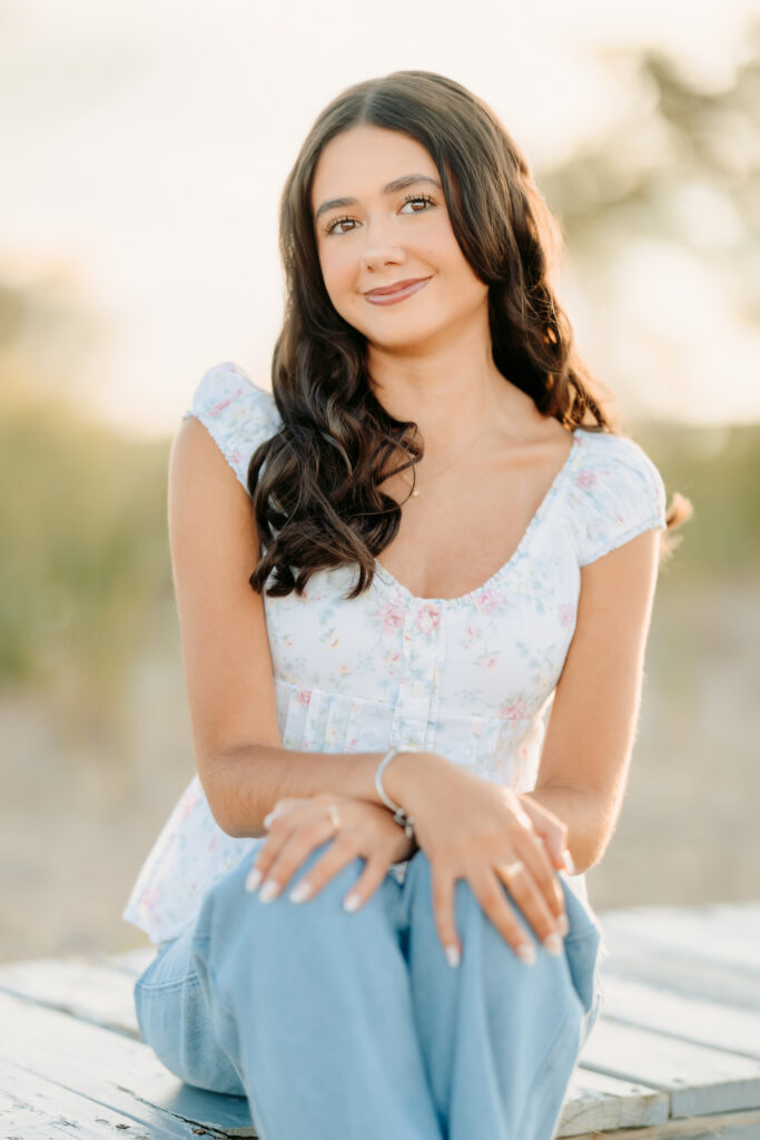 High school senior girls sitting on a piece of driftwood during her senior photos on Plim Island, Newburyport, MA